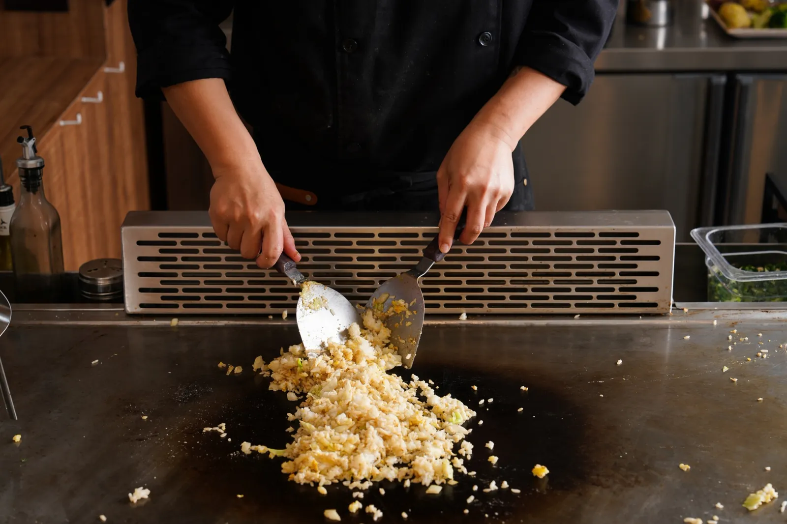 A chef working a large batch of fried rice in the middle of the griddle with two spatulas