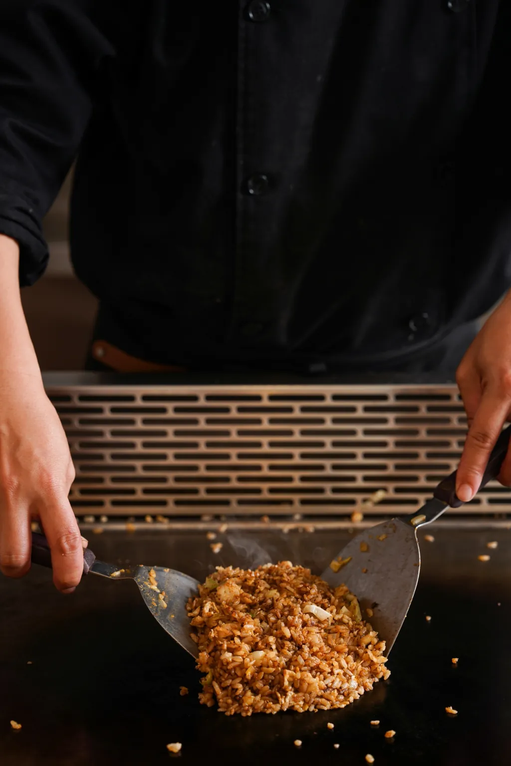 A chef working the rice with a spatula in each hand